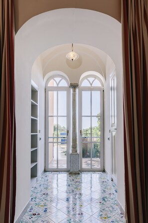 Un pasillo con suelo de baldosas, un candelabro y vistas a través de un ventanal.