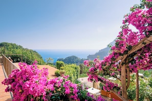Una terraza con flores rosadas, vista al mar y una pérgola de madera.
