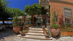 Un patio con escalones que conducen a la entrada de un edificio, rodeado de plantas en macetas y asientos al aire libre.