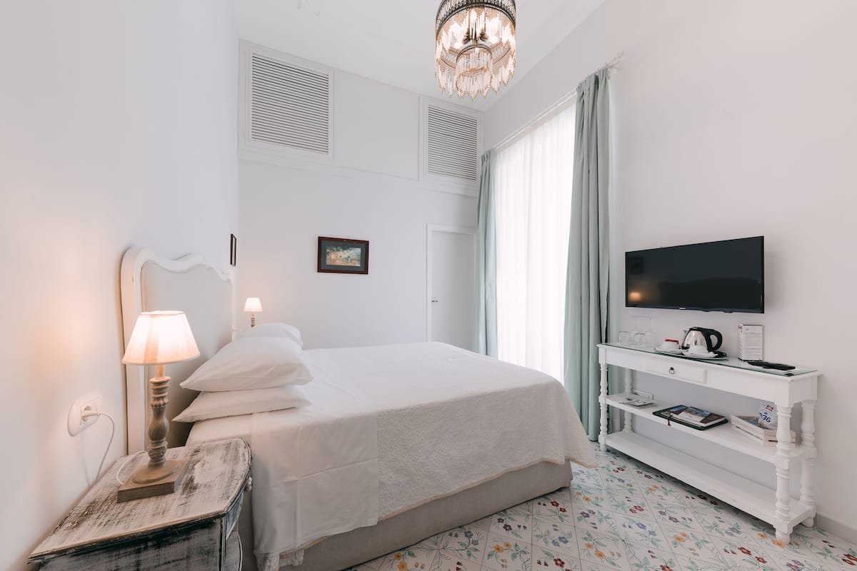 A neatly arranged hotel room with a bed, bedside lamp, TV, and a small white console table.