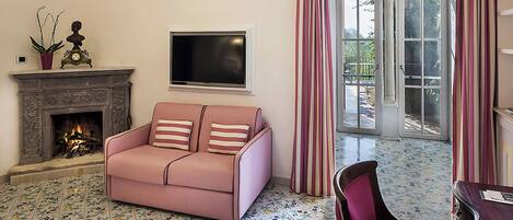 Un salon avec un canapé rose, une cheminée, un téléviseur à écran plat et un coin repas comprenant une chaise et une table.