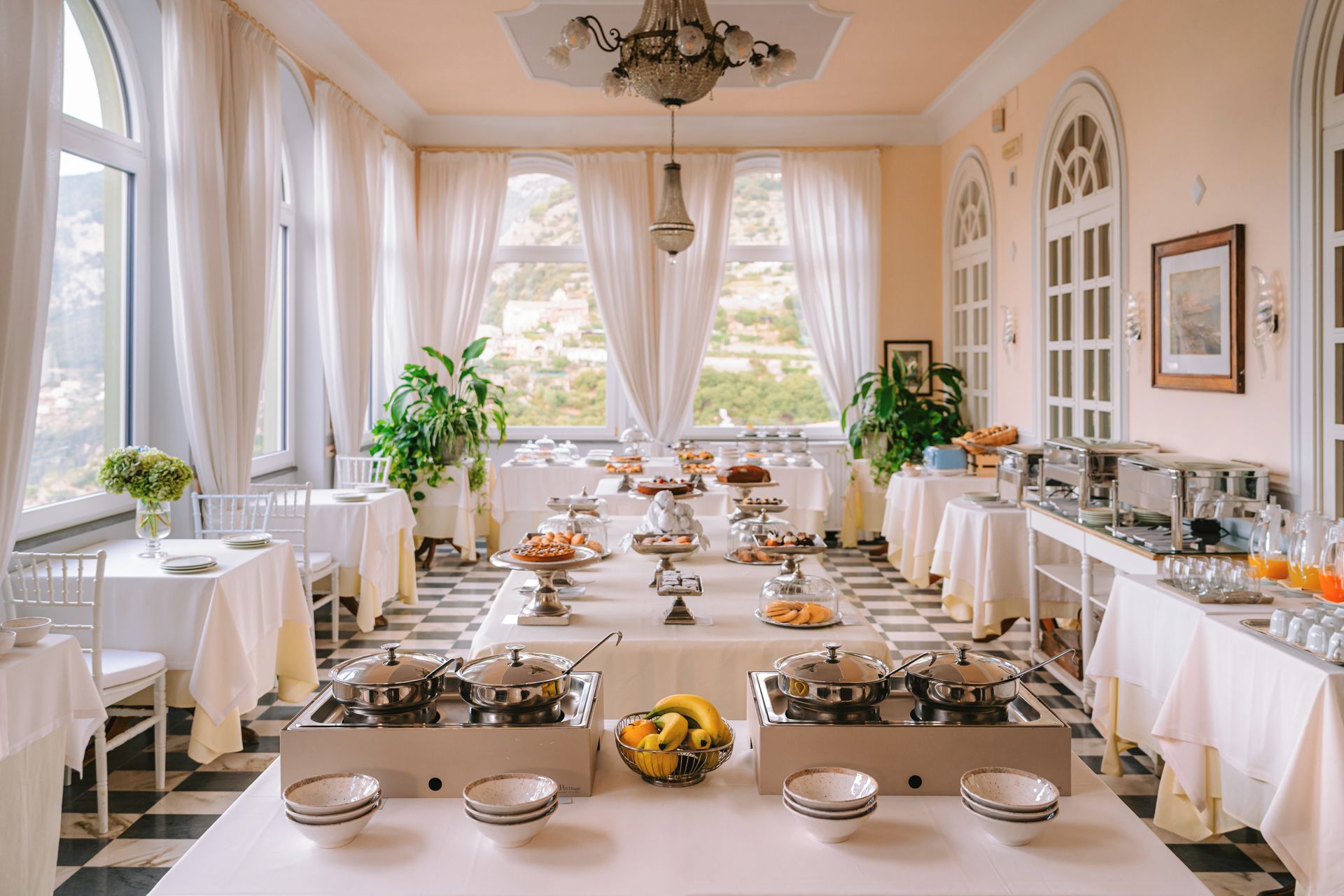 A hotel dining area with multiple tables, a buffet setup, and a view of the outdoors.