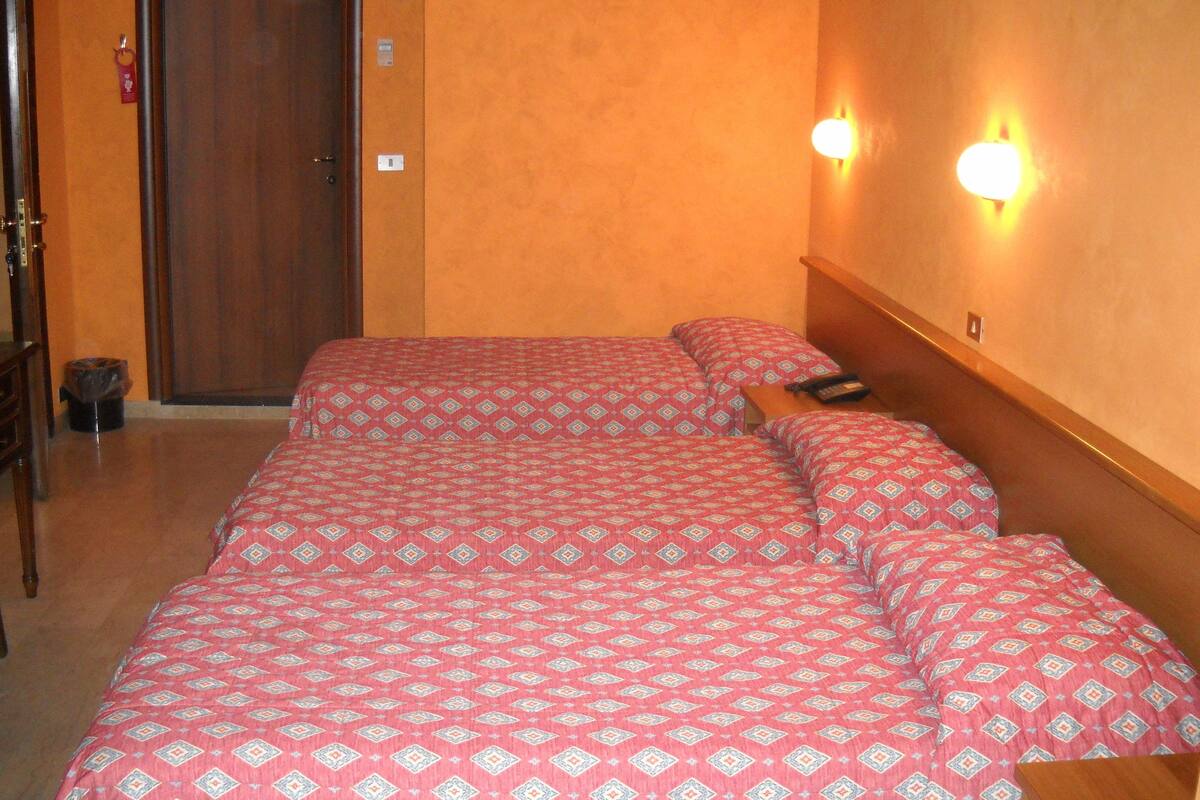 Una habitación de hotel con una cama, una puerta de madera y dos luces fijadas a la pared.