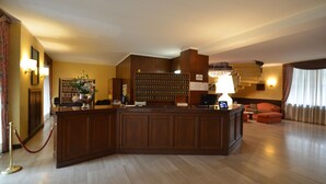 A reception area with a wooden desk, a bookshelf, a chandelier, and a seating area with a sofa and armchairs. - Euro Motel (Nichelino)