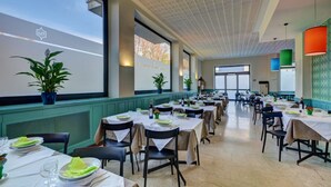 A spacious dining area with multiple tables set for meals, large windows, and potted plants. - Euro Motel (Nichelino)