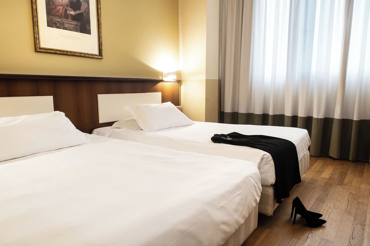A hotel room with two beds, a framed picture on the wall, and a window with curtains.
