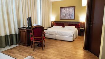 Une chambre d’hôtel avec un plancher en bois, un bureau avec un ordinateur, une chaise rouge, un lit avec une literie blanche et un tableau accroché au mur.