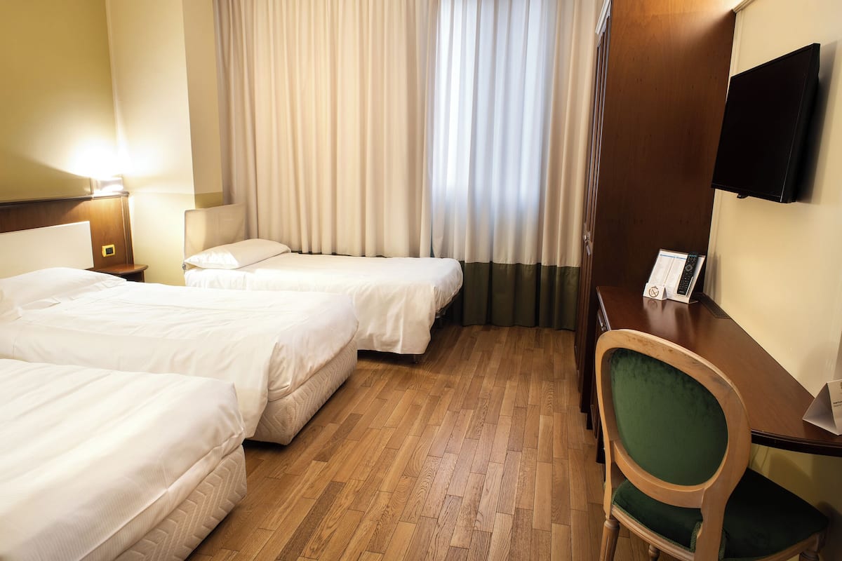 A hotel room with two beds, a wooden desk, a chair, a TV, and a window with curtains.