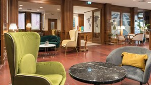 A lobby with green and grey armchairs, a marble table, and wooden decor. - Hotel Dei Congressi (Rome)
