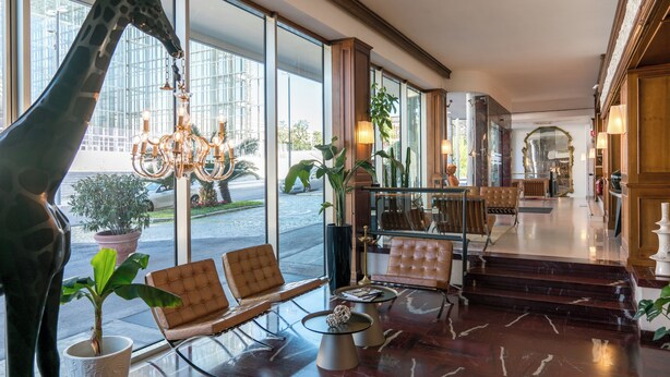 A lobby with a giraffe sculpture, leather chairs, a chandelier, and large windows. - Hotel Dei Congressi (Rome)