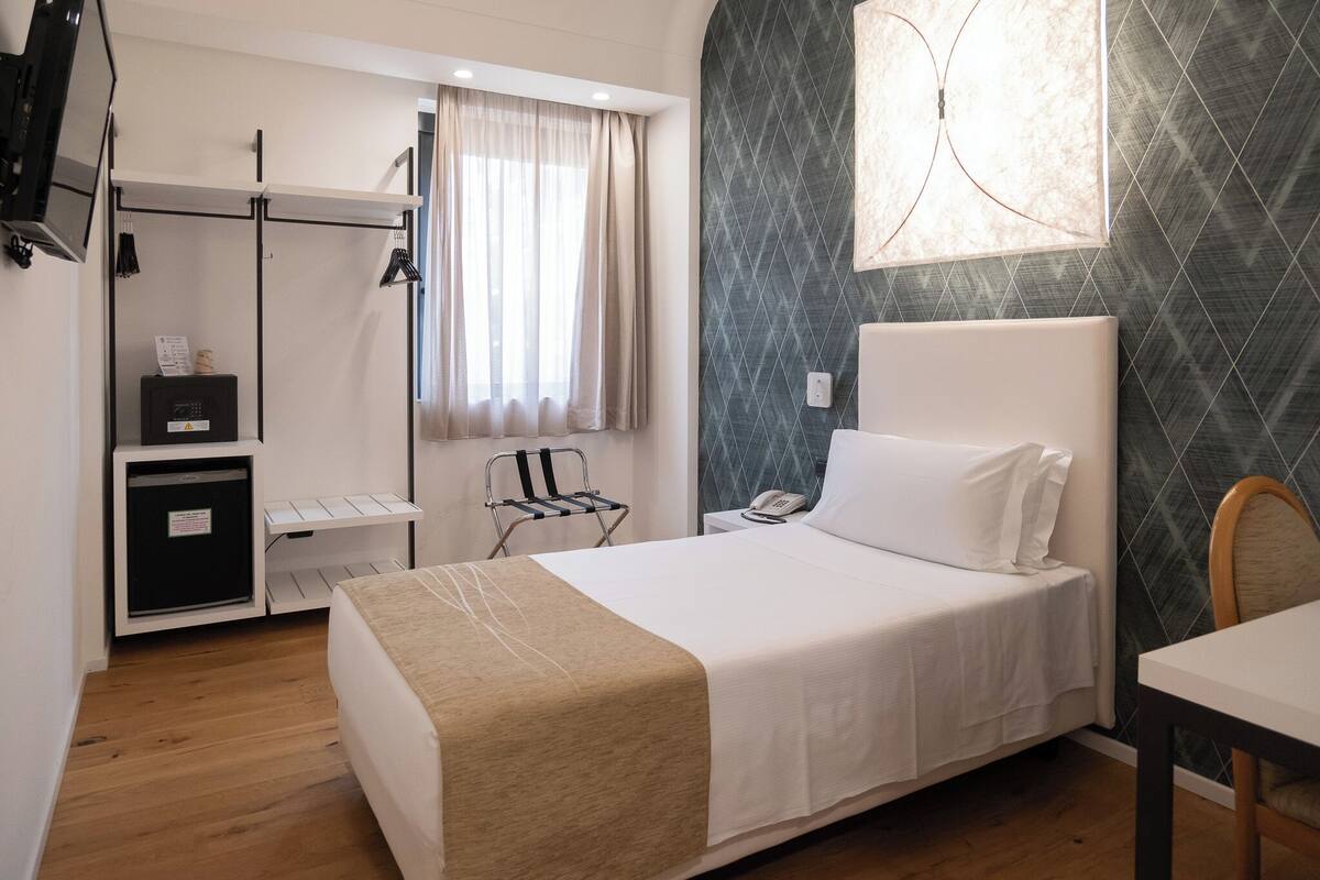 A hotel room with a bed, a desk, a chair, a wardrobe, and a window with curtains.
