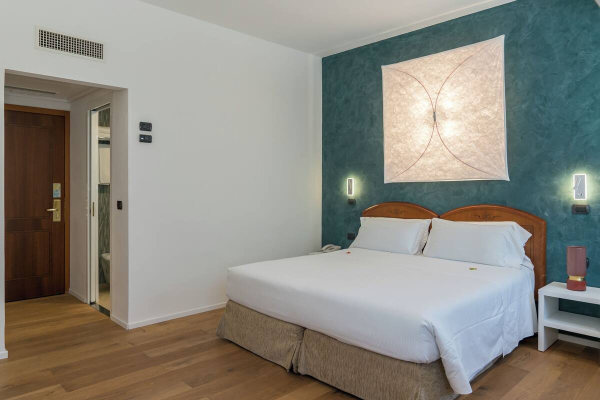 A neatly arranged bedroom with a bed, bedside tables, and a wall-mounted light fixture.