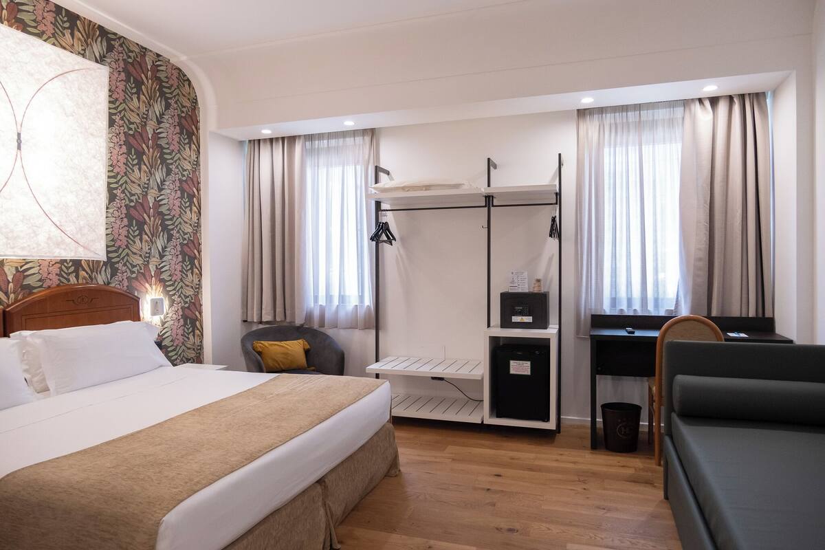 A hotel room with a bed, a desk, a chair, a small cabinet, and a wardrobe.