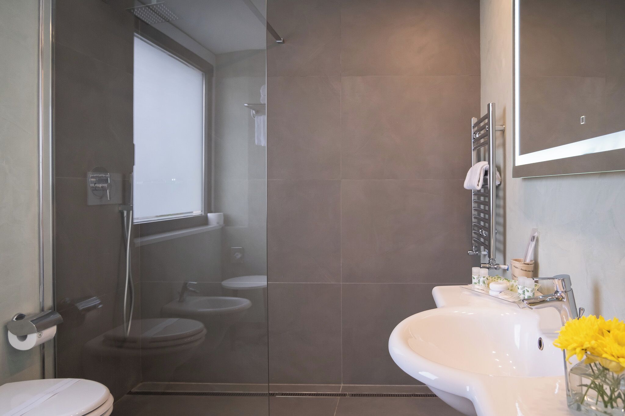 Un baño moderno con ducha envuelta en vidrio, un lavabo blanco con espejo y un inodoro.