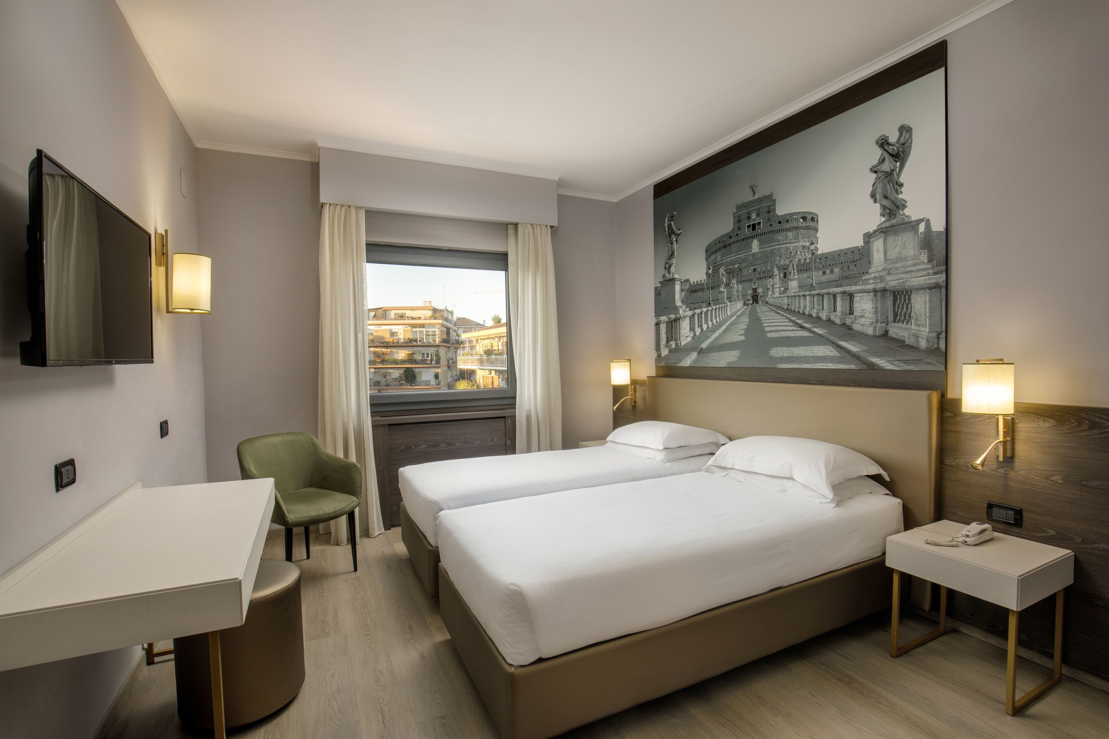 A hotel room with two beds, a desk, a chair, a TV, and a large painting of a historical building.