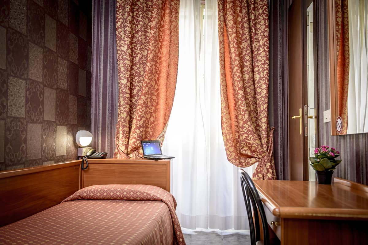 A hotel room with a wooden bed, a desk with a laptop, a telephone, and a potted plant.