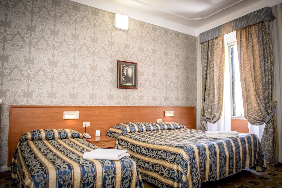A hotel room with two beds, a framed picture on the wall, and a window with curtains.