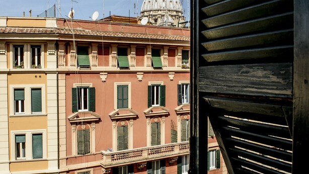 Un immeuble à plusieurs étages, surmonté d’un dôme et doté de balcons, une rue avec des terrasses, et un ciel dégagé.