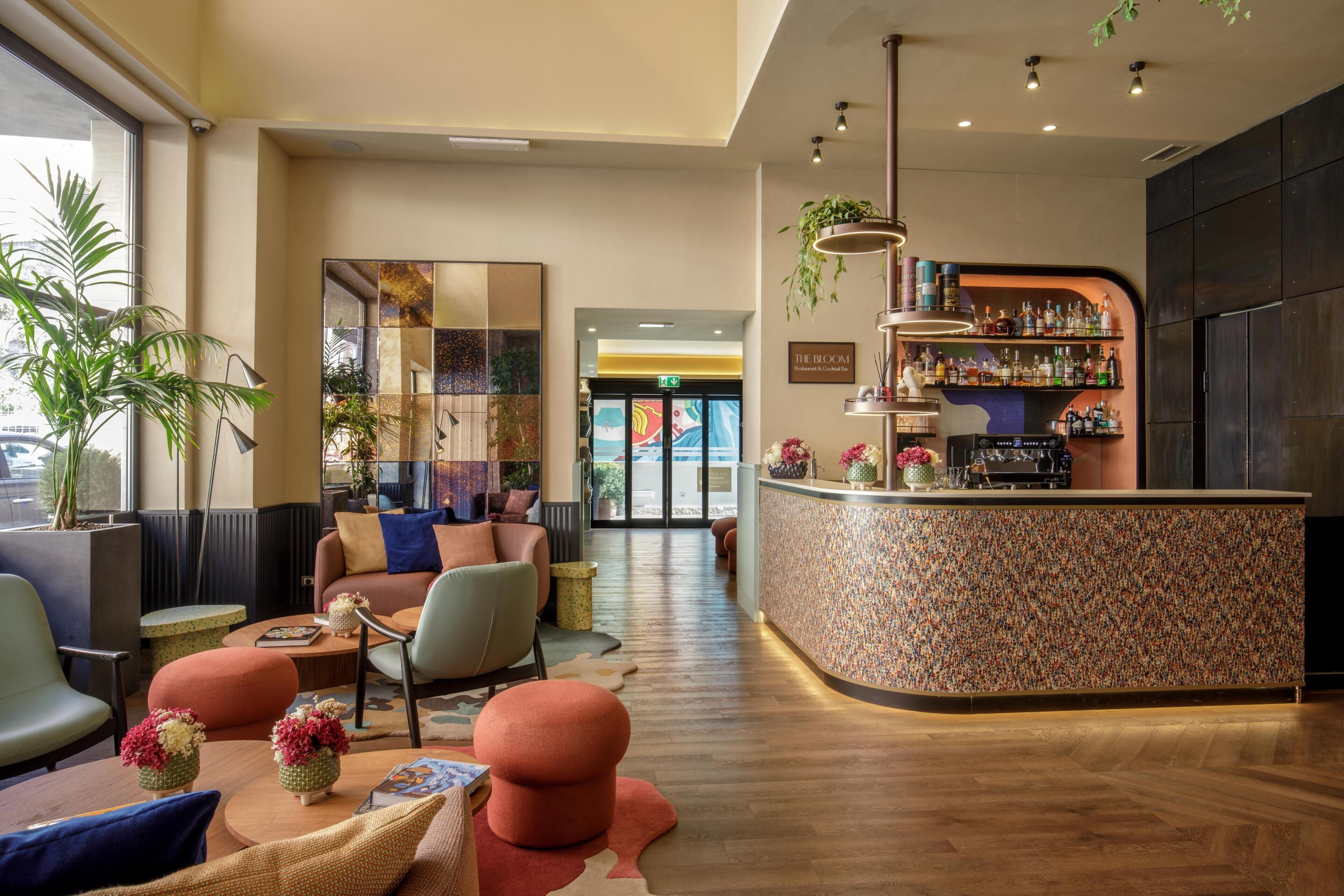 A modern bar area with a curved counter, seating with colorful cushions, and a variety of plants.