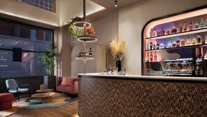 A modern bar area with a circular light fixture, a coffee machine, and a variety of bottles on shelves. - The Spring House Hotel Rome Vatican, Tapestry Collection Hilton (Rome)