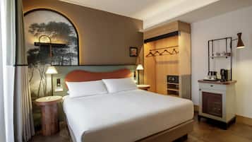 A hotel room with a large bed, bedside tables, a wardrobe, a small desk with a lamp, and a view of trees through a window.