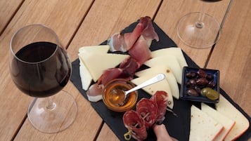 A wooden table with a black slate board holding cheese, cured meats, olives, and a glass of red wine.