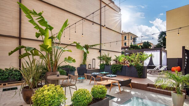 A modern outdoor patio with a pool, seating areas, and lush greenery. - The Spring House Hotel Rome Vatican, Tapestry Collection Hilton (Rome)