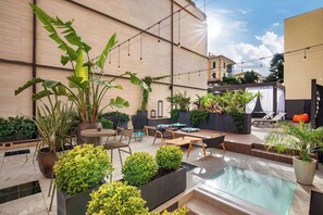Un patio moderno al aire libre con mobiliario, plantas y una piscina.