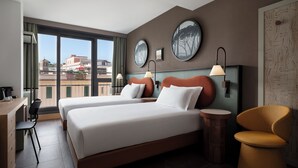 A hotel room with two beds, a desk, and a chair. There are large windows with a view of buildings outside. - The Spring House Hotel Rome Vatican, Tapestry Collection Hilton (Rome)