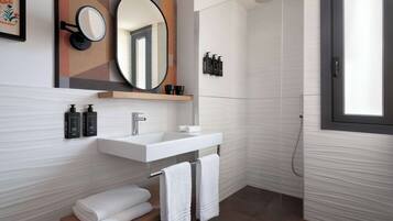 Un bagno moderno con un lavandino bianco, uno specchio e una doccia. Asciugamani e articoli da toilette sono presenti sul lavandino.