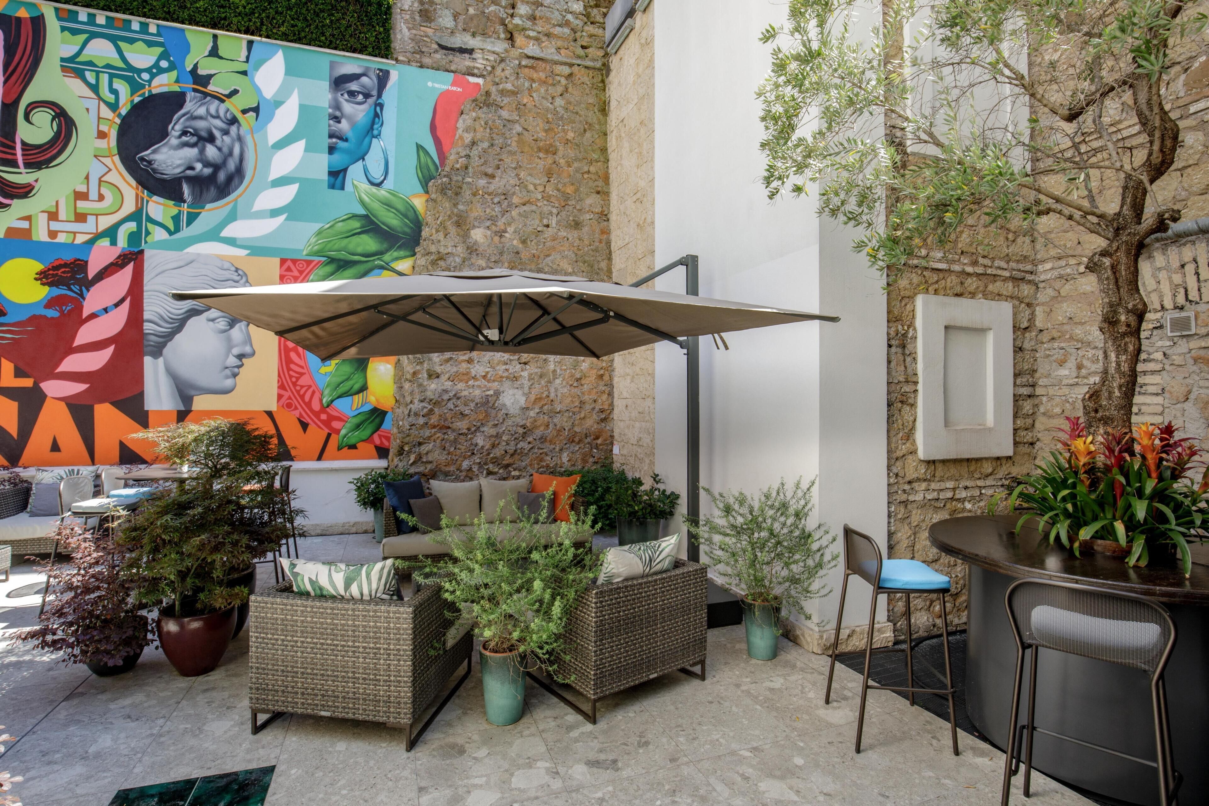 An outdoor seating area with wicker furniture, a mural, and a tree.