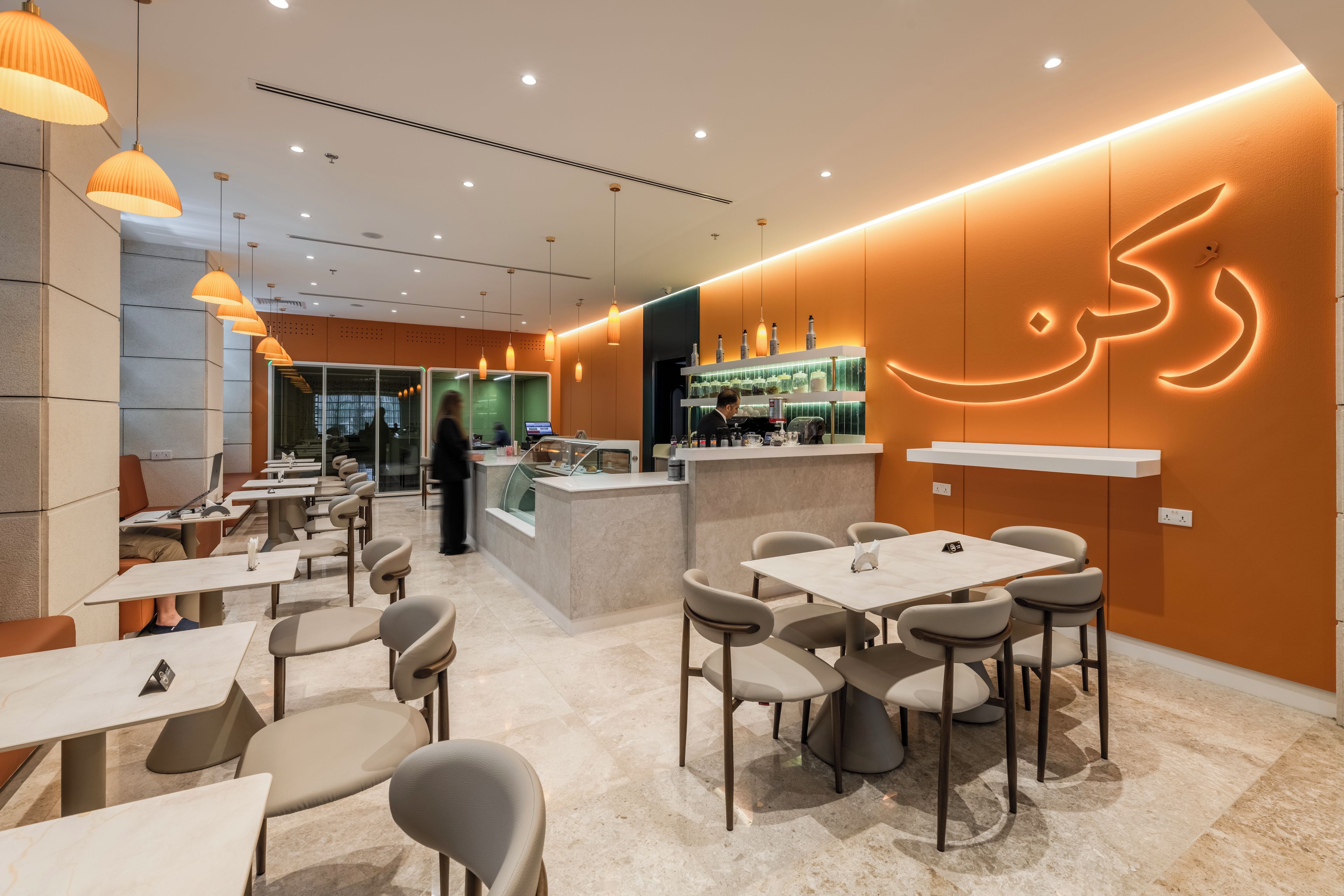 Un café moderne avec un intérieur comprenant des tables et des chaises, un bar et un grand mur décoratif éclairé.