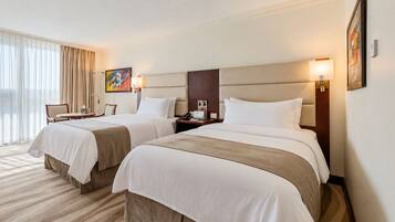 Habitación de hotel con dos camas, un escritorio, una silla y un ventanal con cortinas.