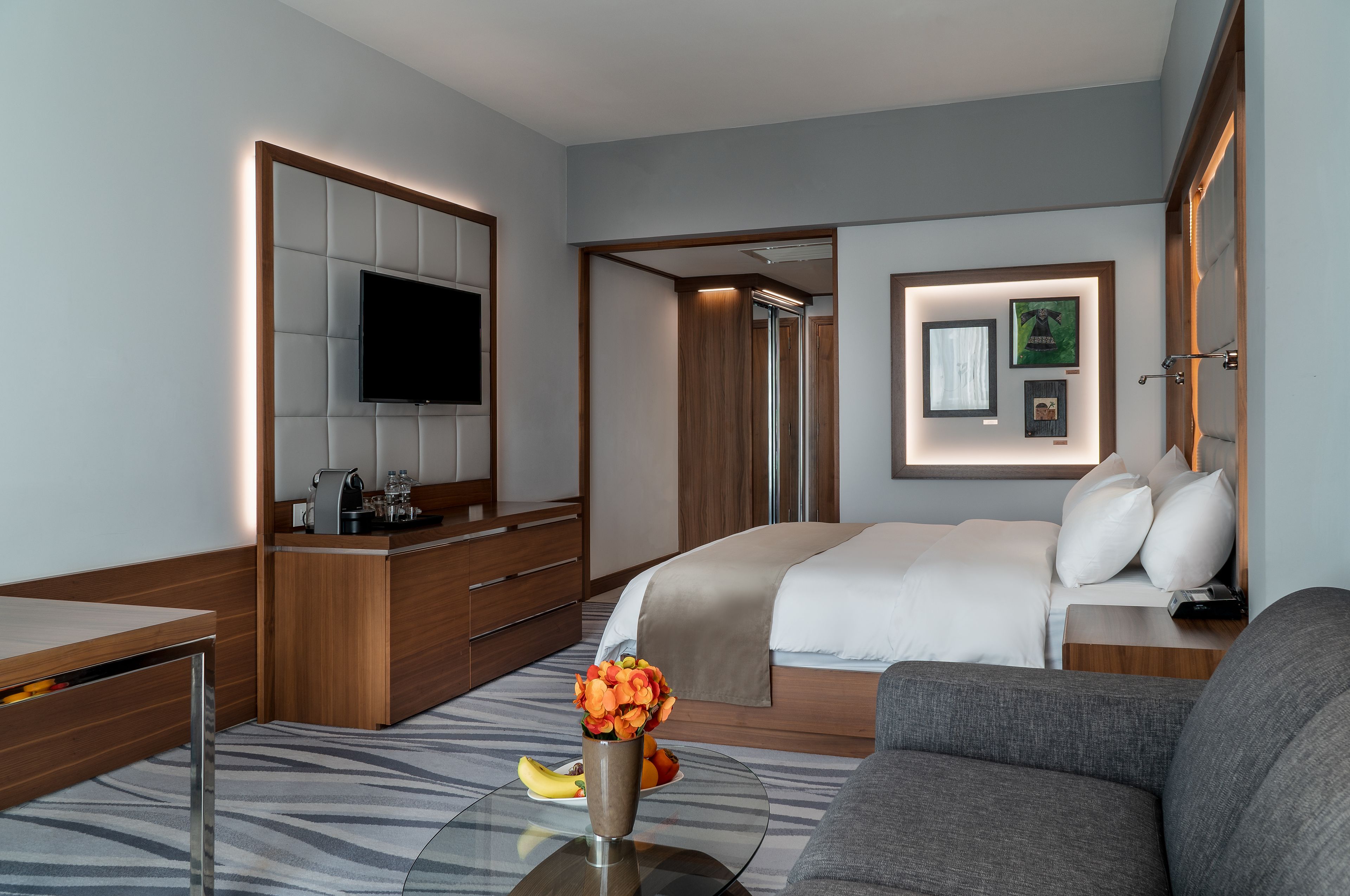 A modern hotel room with a bed, a TV, a desk, and a sofa.
