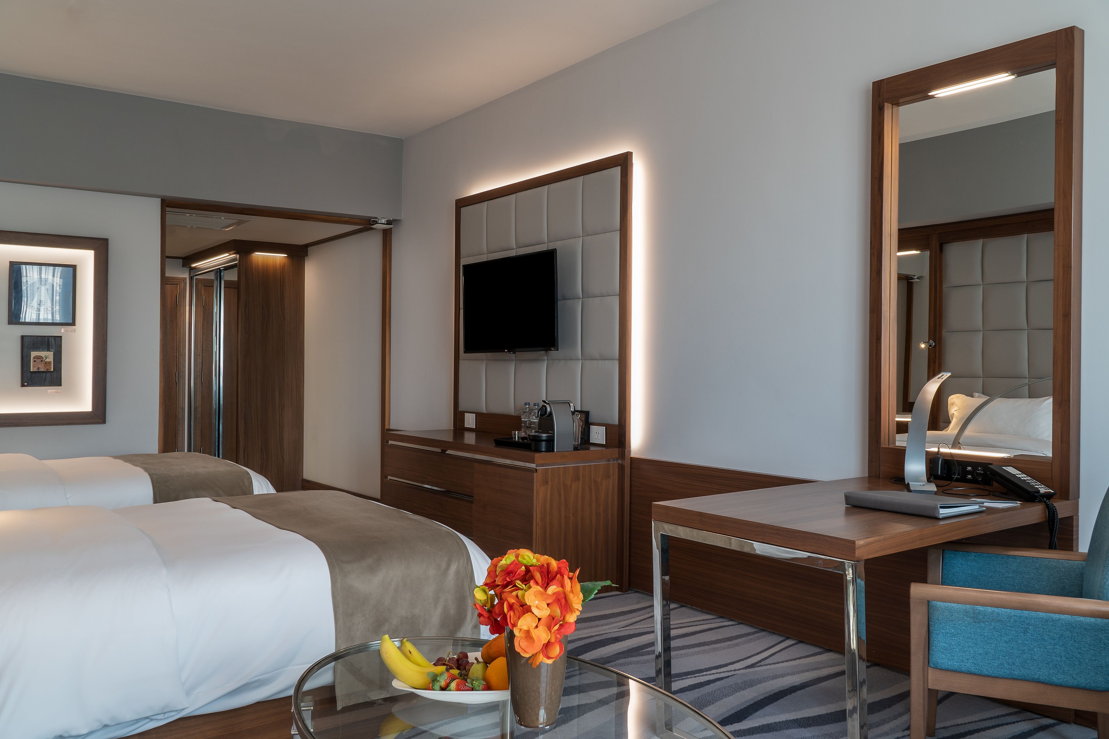 A hotel room with two beds, a desk with a chair, a TV, and a mirror.