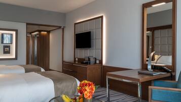 Habitación de hotel con dos camas, un escritorio con una silla, un televisor y un espejo.