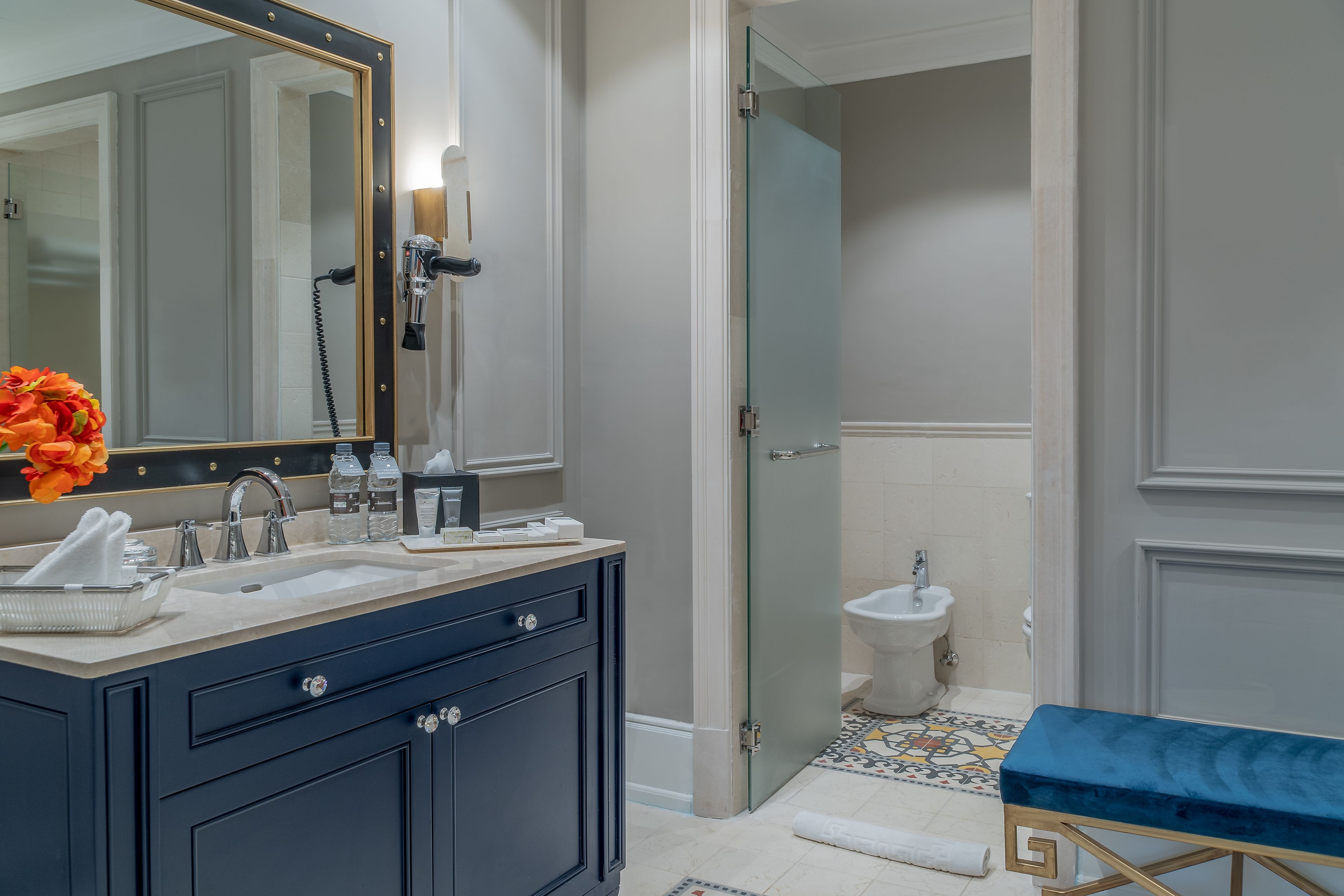 A bathroom with a large mirror, a sink, a handheld showerhead, a bidet, and a bench.