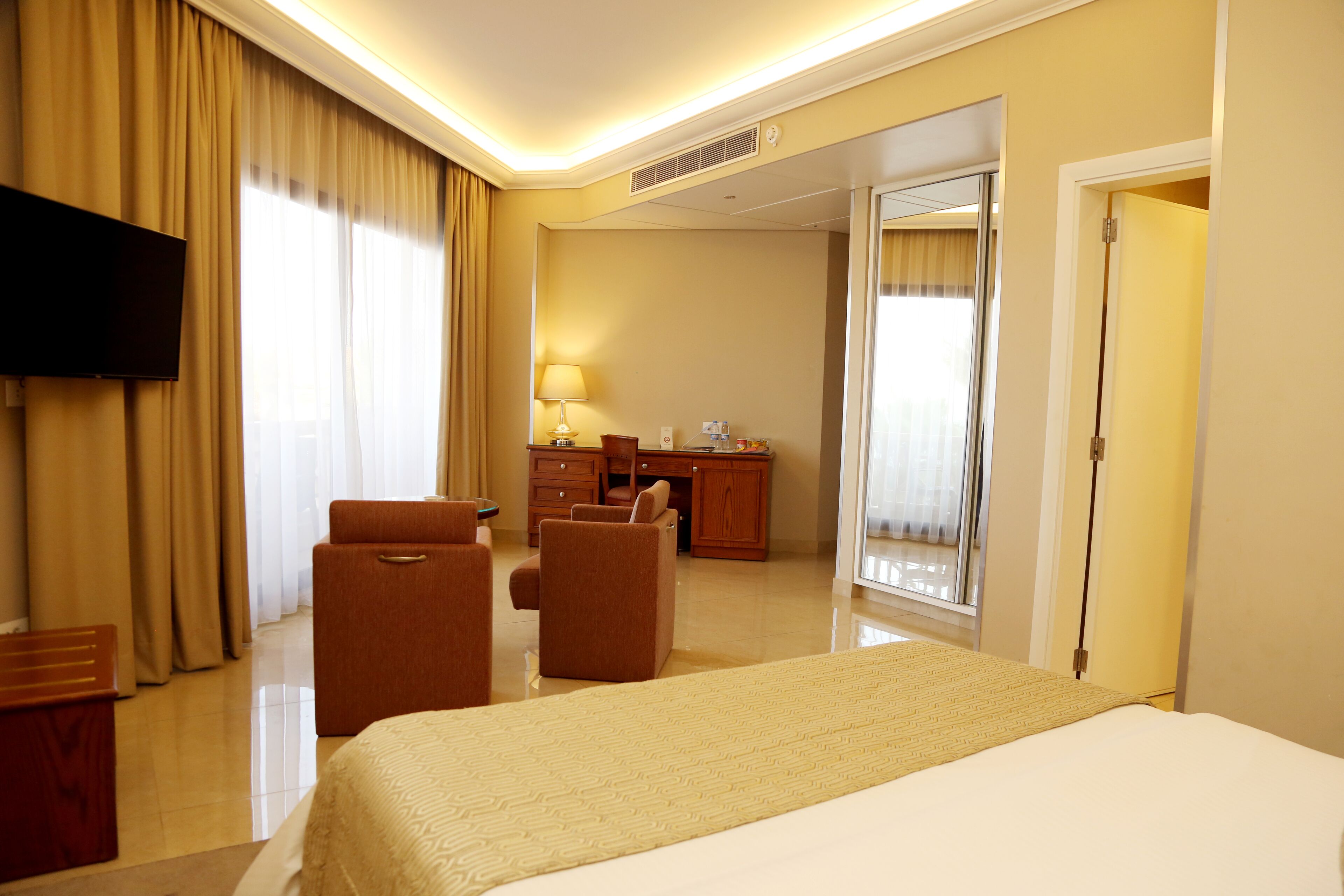 A hotel room with a large bed, a desk, a chair, a television, and a bathroom visible through an open door.