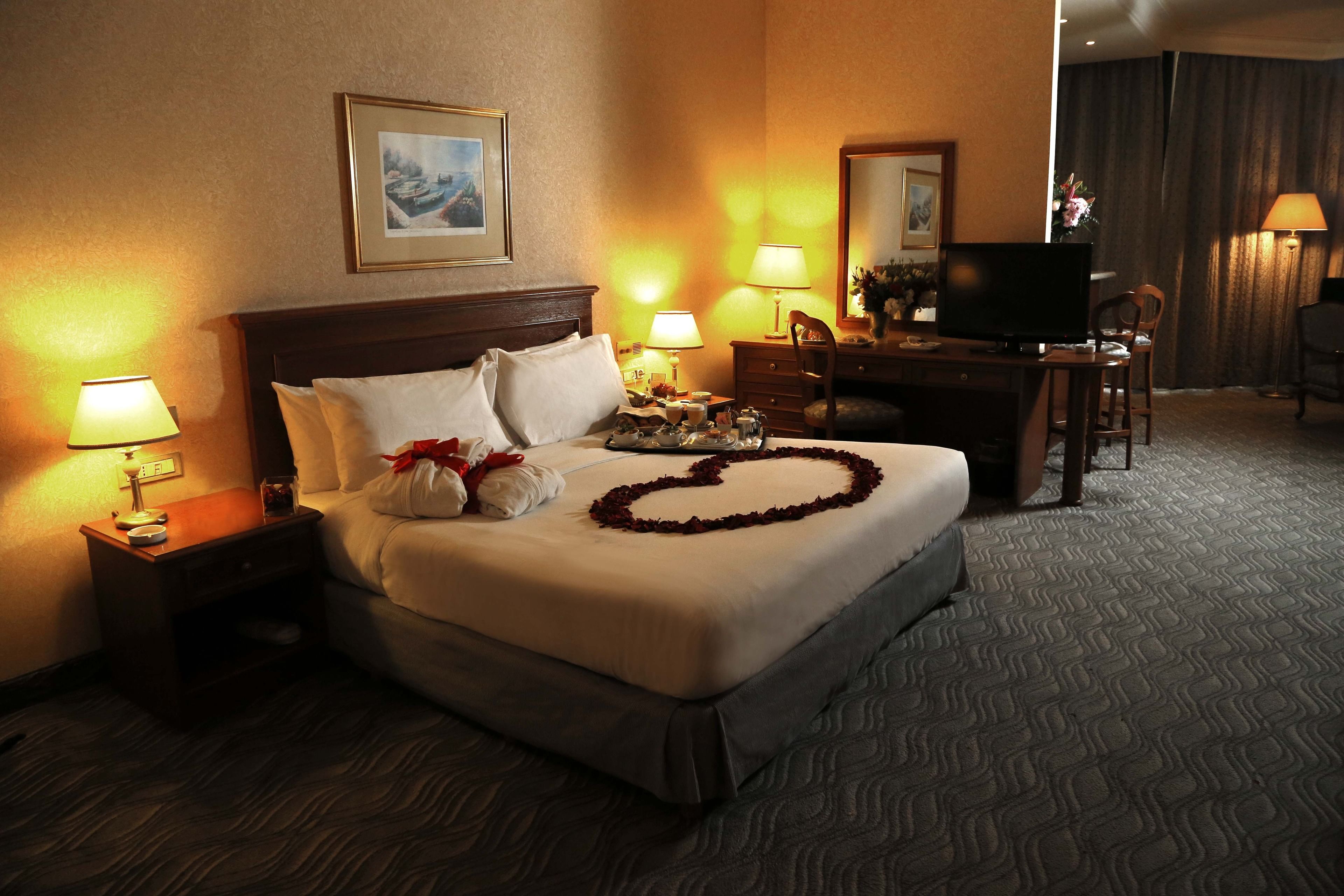 A hotel room with a large bed, two bedside tables with lamps, a flat-screen TV, a desk with a chair, and a mirror.