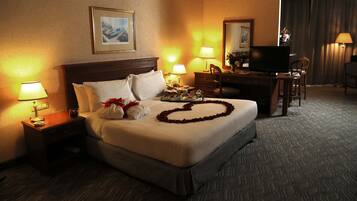 A hotel room with a large bed, two bedside tables with lamps, a flat-screen TV, a desk with a chair, and a mirror.