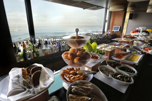 A buffet table with various food items and a view of the ocean through large windows. - The Bayview Hotel (Beirut)