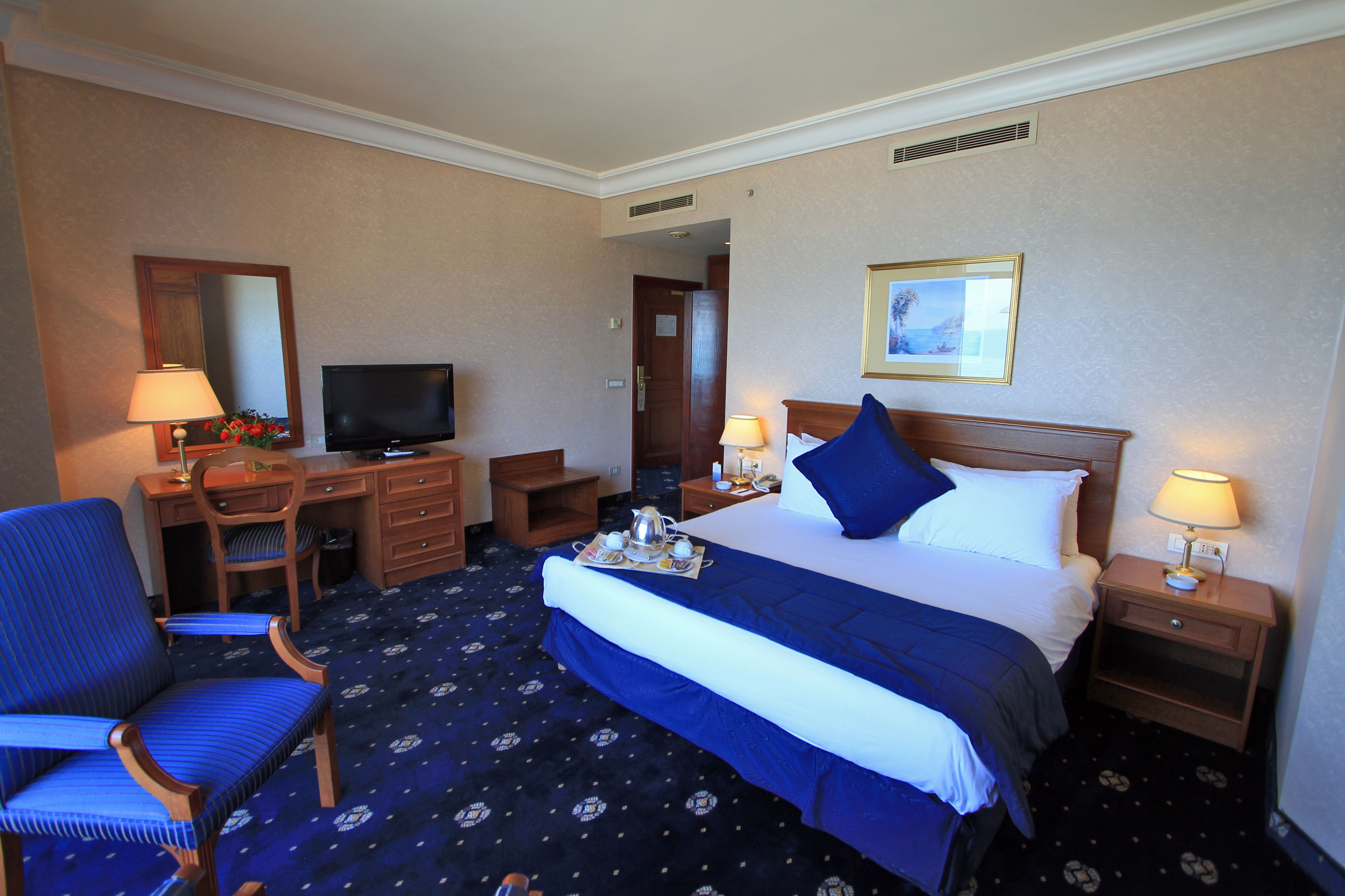 Ein Hotelzimmer mit einem Bett, einem Schreibtisch mit Fernseher, einem Sessel und einem Nachttisch mit Lampe.