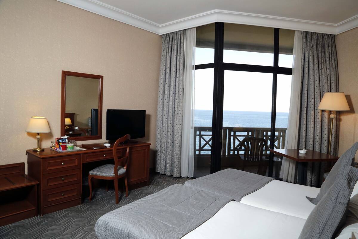 Habitación de hotel con cama, escritorio, silla, televisión y balcón con vistas al mar.