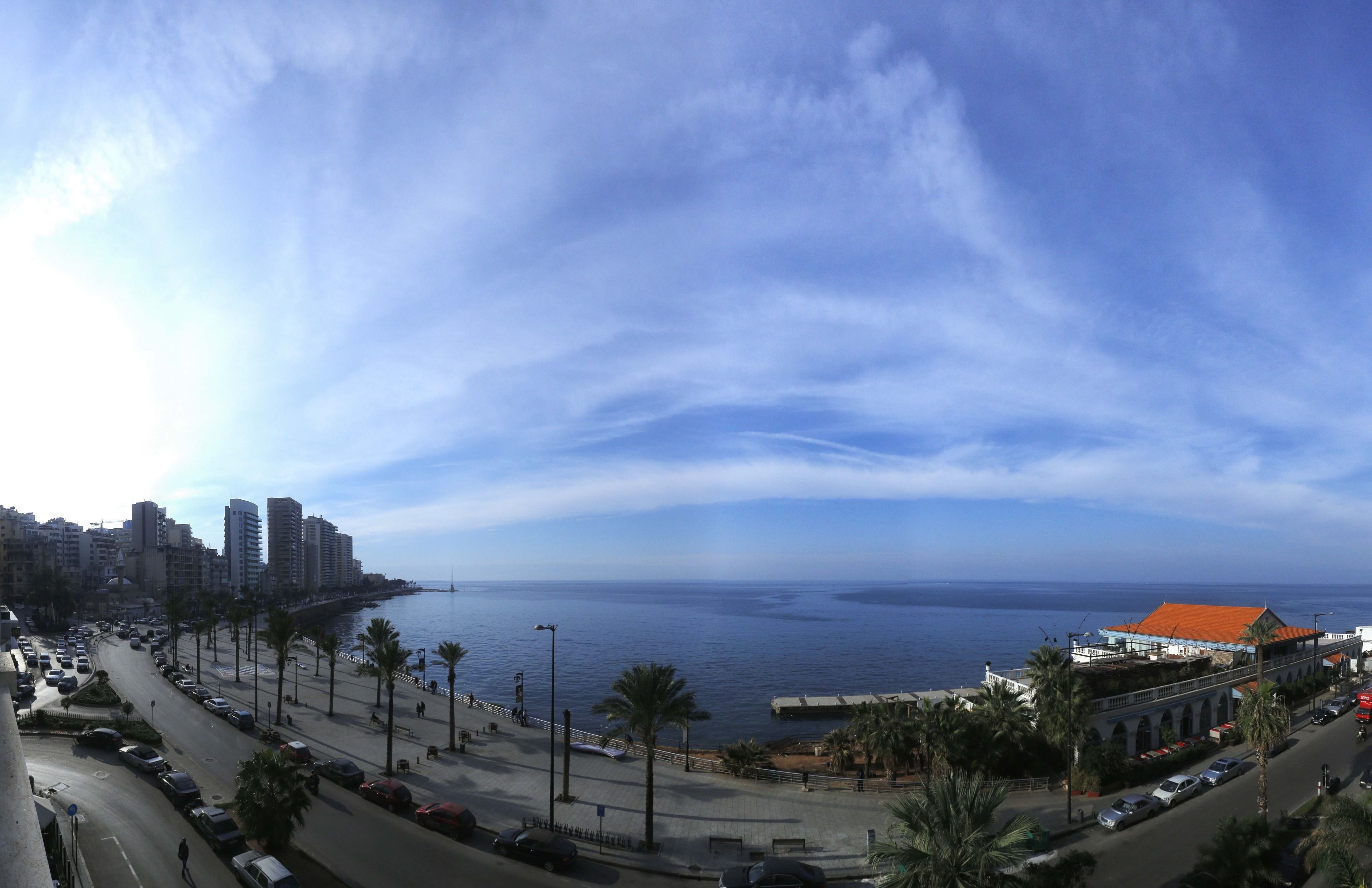 Un paisaje urbano costero con una avenida amplia, palmeras y edificios a lo largo del frente marítimo.