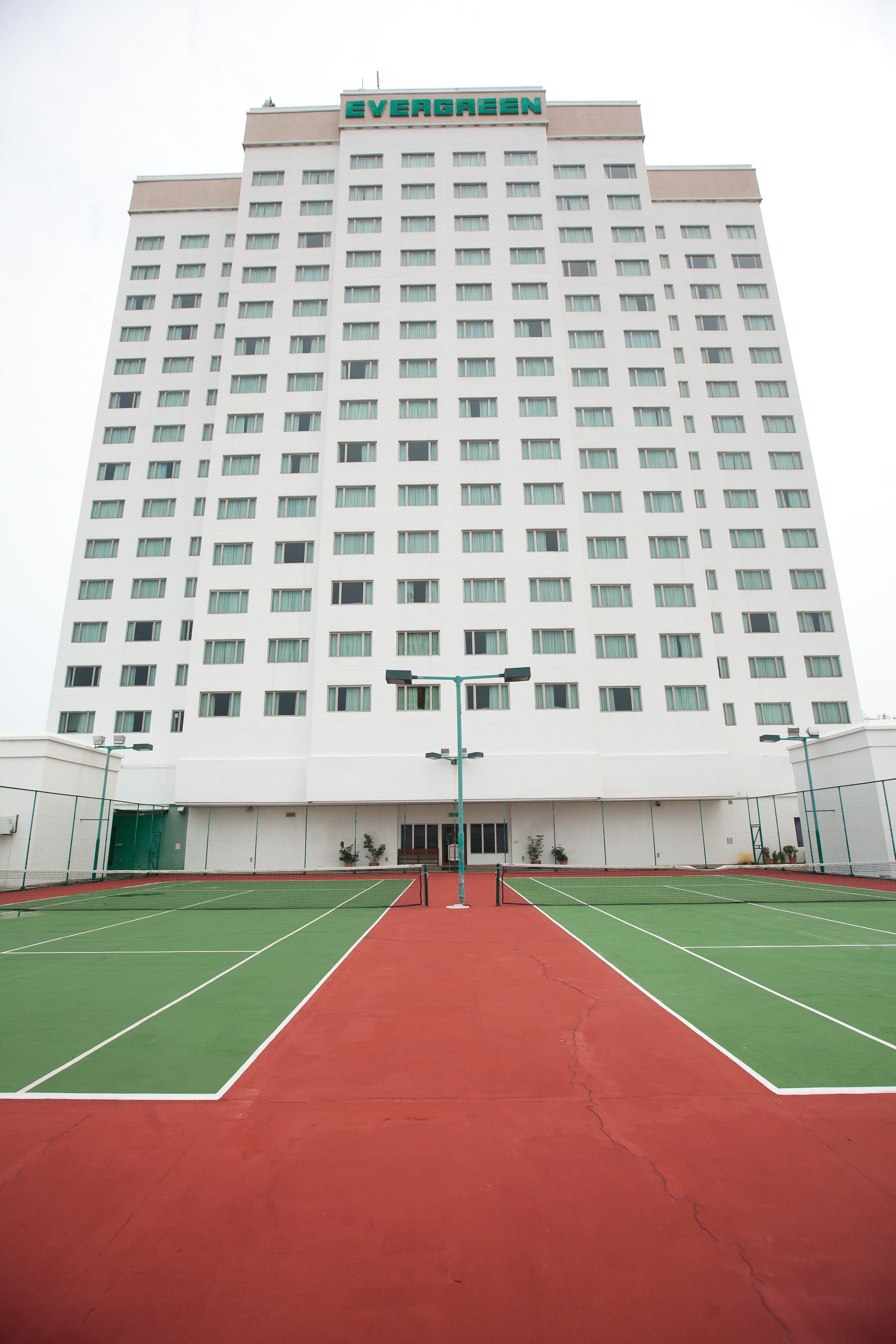 A large hotel building with multiple floors and a tennis court in the foreground.