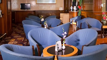 Un hall d’hôtel avec un espace salon comprenant des chaises bleues et une table ronde sur laquelle est posé un vase de fleurs.