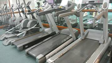 En rad löpband i ett gym, med en spegelvägg och en tv-skärm i bakgrunden.