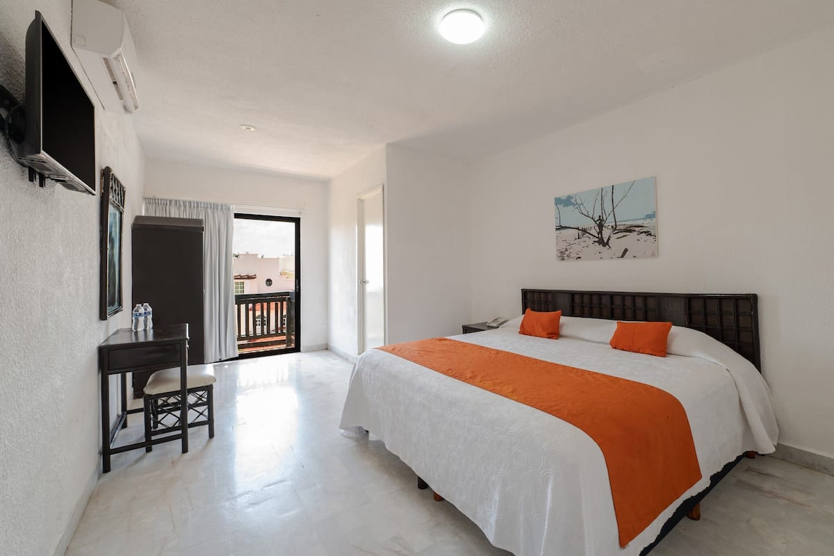 Ett sovrum med en säng, ett skrivbord, en stol, en tv och en tavla på väggen.