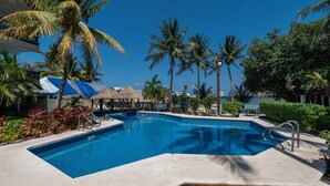 A swimming pool with a clear blue water, surrounded by palm trees and a thatched-roof structure. - Hotel Imperial Laguna Faranda (Cancun)