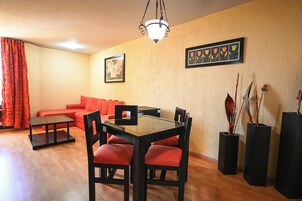 Una sala de estar con un sofá rojo, una mesa de comedor con cubierta de vidrio y sillas, una mesita negra y una cortina roja.